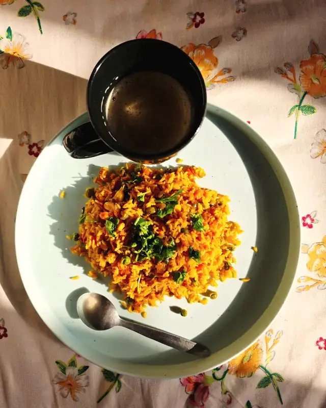 A comforting plate of vegetable pulao beside a cup of tea on a floral tablecloth