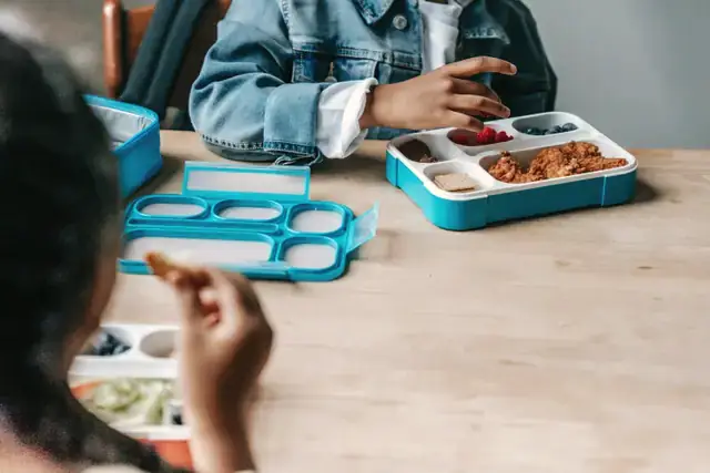 Children opening blue tiffin boxes at a school table