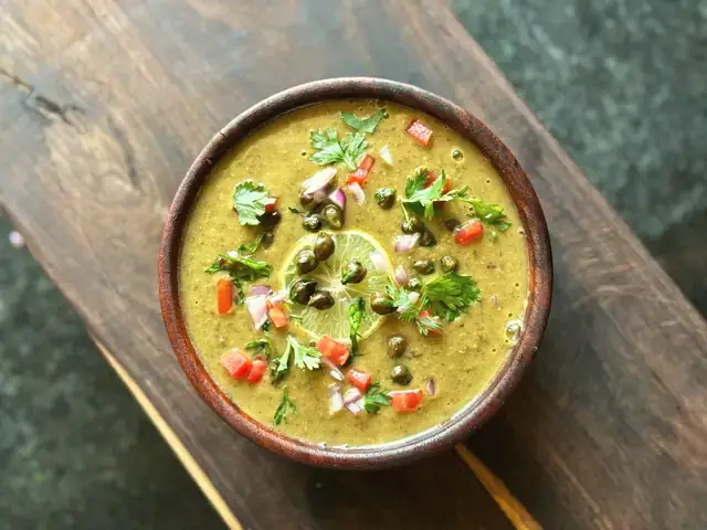 A wooden bowl of green moong dal topped with coriander and diced tomato